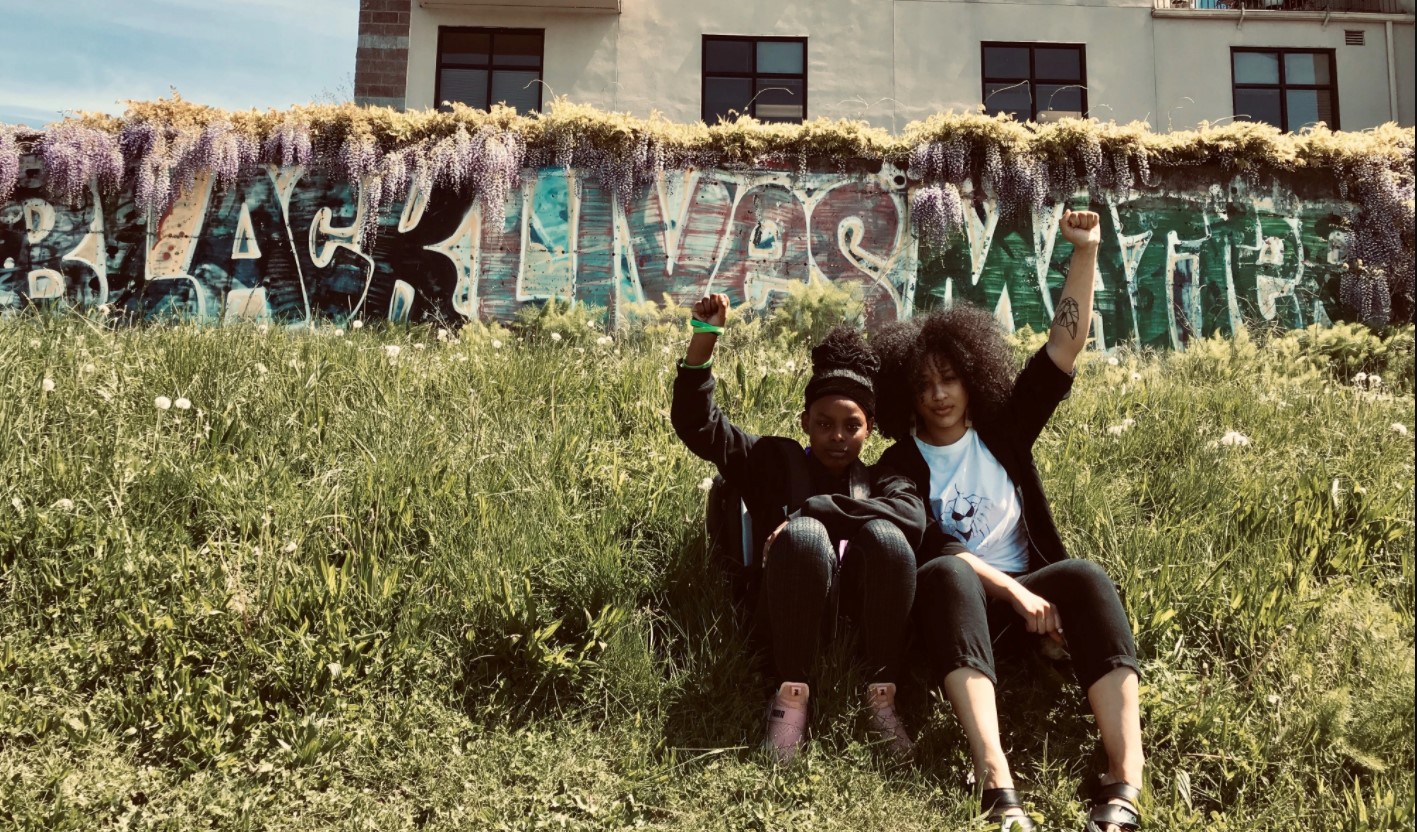 Janell and a youth pose with their fists in the air in front of a wall that says "Black Lives Matter"